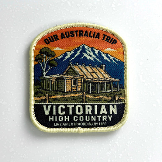 A vintage-style travel pinback badge featuring a mountain cabin scene with the text 'OUR AUSTRALIA TRIP' at the top and 'VICTORIAN HIGH COUNTRY' at the bottom, displayed on a white textured surface.